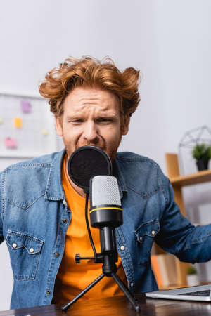 tense redhead announcer in denim shirt speaking in microphone at workplaceの写真素材