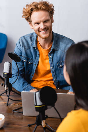 selective focus of excited redhead radio host interviewing brunette woman in studioの写真素材