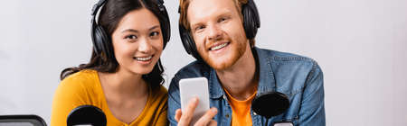 panoramic concept of redhead radio host holding smartphone while looking at camera together with...