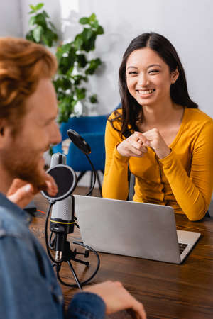 selective focus of excited asian interviewer looking at guest in radio studioの写真素材