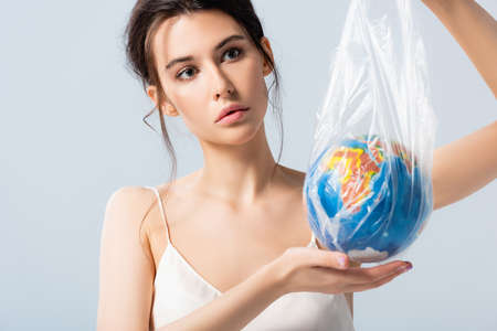 young woman in silk dress holding plastic bag with globe isolated on white, ecology concept