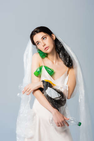 woman with plastic bag on head standing in silk dress with empty bottles isolated on gray, ecology conceptの写真素材