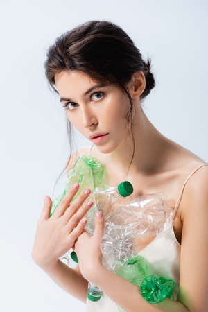 brunette woman holding plastic bottles and looking at camera isolated on white, ecology concept