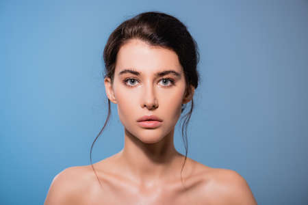 young and naked woman looking at camera isolated on blueの写真素材