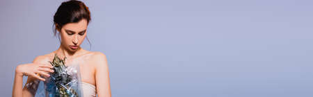 panoramic crop of brunette woman holding pineapple in polyethylene isolated on gray, ecology concept