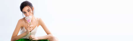 panoramic shot of brunette woman smelling pink flower in plastic wrap isolated on white, ecology conceptの写真素材