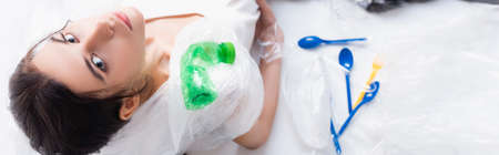 horizontal image of woman sitting near empty bottles, plastic bags and spoons on white, ecology...