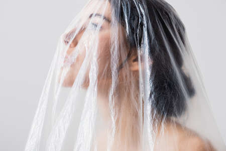 young brunette model looking through polyethylene isolated on gray, ecology conceptの写真素材