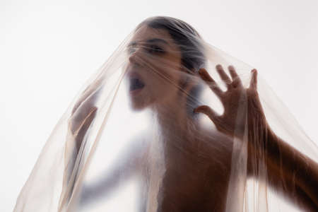 trapped brunette woman screaming through polyethylene isolated on white, ecology conceptの写真素材