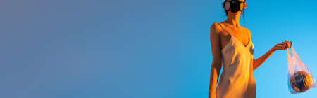panoramic crop of woman in gas mask holding plastic bag with globe on blue, ecology concept