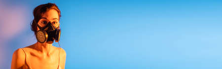 panoramic concept of brunette woman in gas mask looking at camera on blueの写真素材