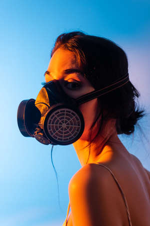 young and brunette woman in gas mask on blueの写真素材