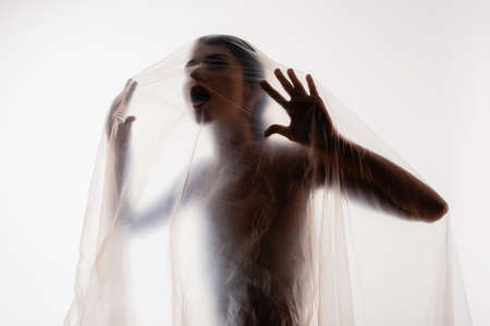 young trapped woman screaming through polyethylene isolated on white, ecology conceptの写真素材