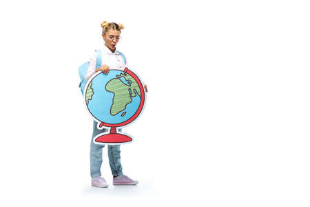 full length view of amazed schoolgirl in eyeglasses holding paper cut globe while standing on whiteの写真素材