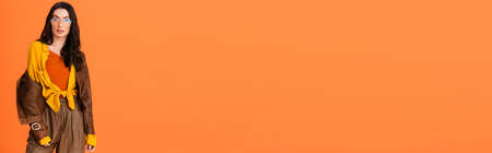 panoramic orientation of woman in autumn outfit and leather jacket posing isolated on orangeの写真素材