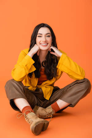 brunette and joyful woman in autumn outfit sitting on orange