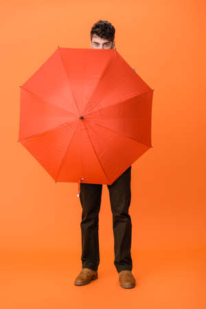 full length of man in brown pants holding umbrella on orangeの写真素材