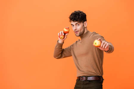 man in autumn outfit holding fresh apples isolated on orangeの写真素材