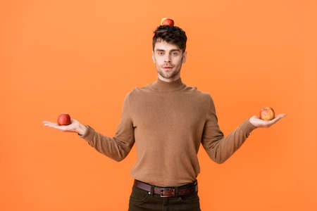 man in autumn outfit holding fresh apples on head and hands isolated on orangeの写真素材