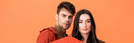 panoramic crop of couple looking at camera isolated on orangeの写真素材