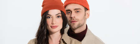 panoramic orientation of fashionable couple in beanie hats looking at camera isolated on white