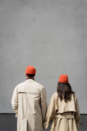 back view of couple in trench coats and hats standing near gray wallの写真素材