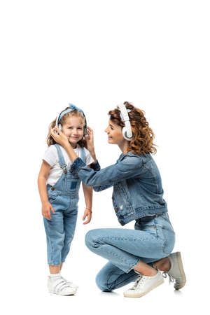 mother and daughter in denim outfits listening music in headphones isolated on whiteの写真素材