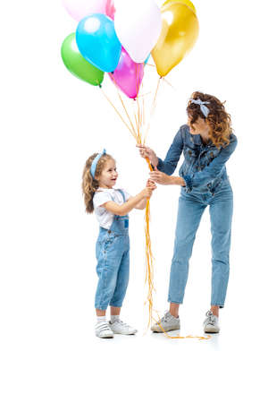 mother and daughter in denim outfits holding colorful balloons isolated on whiteの写真素材