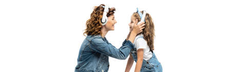 side view of mother and daughter in denim outfits listening music in headphones face to face isolated on white, panoramic shotの写真素材