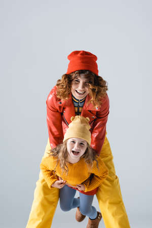 mother and daughter in colorful red and yellow outfits smiling isolated on gray