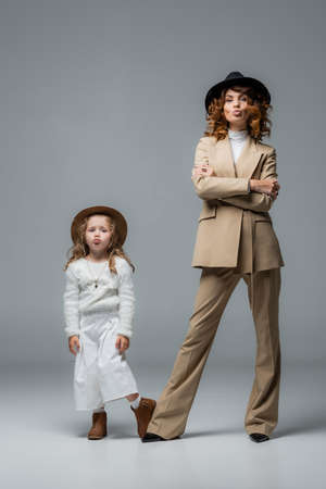 elegant mother and daughter in white and beige outfits showing kiss on grayの写真素材