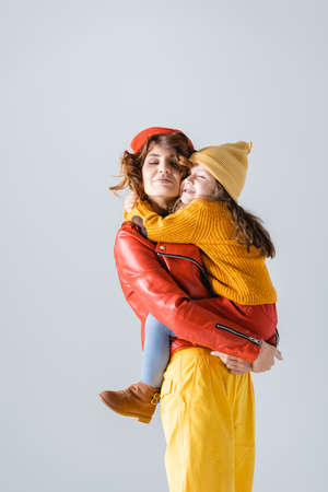 mother and daughter in colorful red and yellow outfits embracing isolated on grayの写真素材