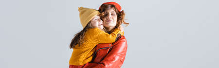 mother and daughter in colorful red and yellow outfits embracing isolated on gray, panoramic shotの写真素材