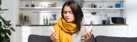 panoramic crop of woman with scarf on neck holding nasal and throat sprays in kitchen