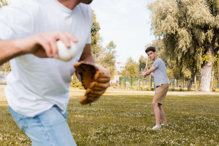 selective focus of teenager son with softball bat looking at father while playing baseball in parkの写真素材