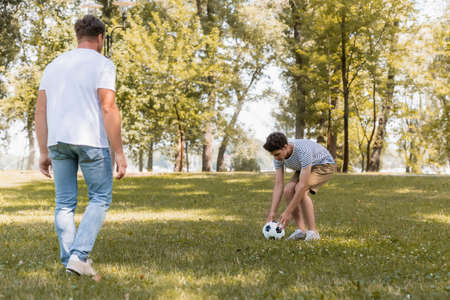selective focus of teenager son touching football near fatherの写真素材