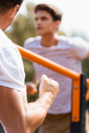 selective focus of father with clenched fist near teenager son exercising on horizontal bars