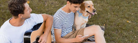 high angle view of man playing acoustic guitar near teenager boy with smartphone and golden...