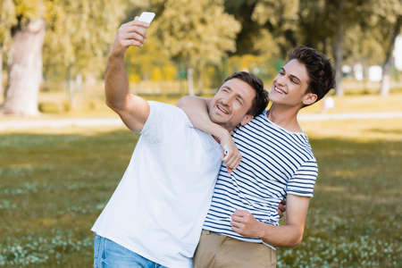 teenager son hugging father while taking selfie in parkの写真素材