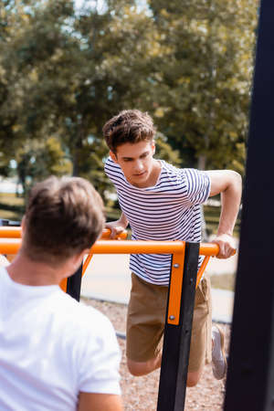 selective focus of teenager boy exercising on horizontal bars near man