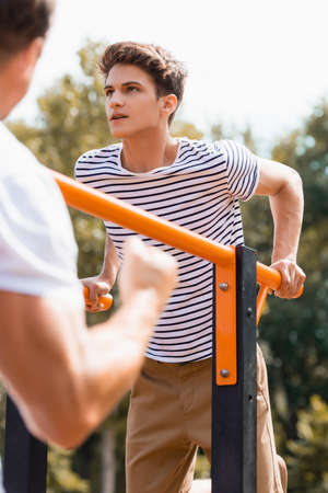 selective focus of teenager boy exercising on horizontal bars near father