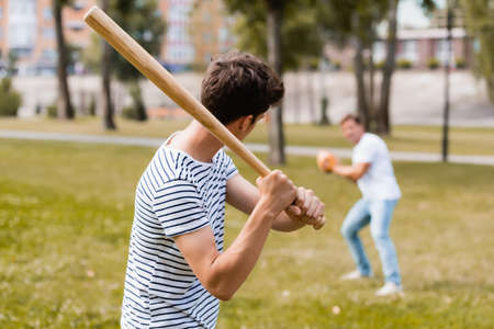 back view of teenager son with softball bat playing baseball with father in parkの写真素材