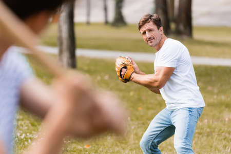 selective focus of concentrated father in leather glove playing baseball with teenager son in parkの写真素材