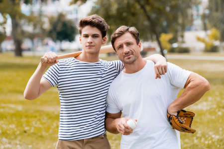 teenager boy with softball bat standing near father in leather glove holding ballの写真素材