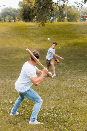back view of father holding softball bat while playing baseball with teenager boyの写真素材
