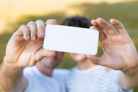 selective focus of smartphone in hands on father and teenager son taking selfieの写真素材
