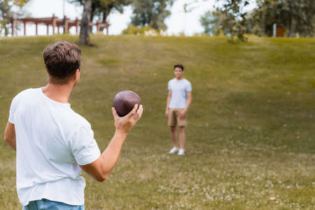 selective focus of father holding rugby ball near teenager son in green parkの写真素材