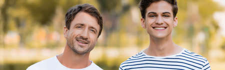 panoramic shot of father and teenager son looking at camera outside