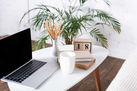 Selective focus of laptop with blank screen, books and cup on coffee tableの写真素材