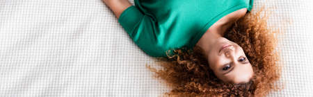 Panoramic concept of young red haired woman looking at camera while lying on bedの写真素材